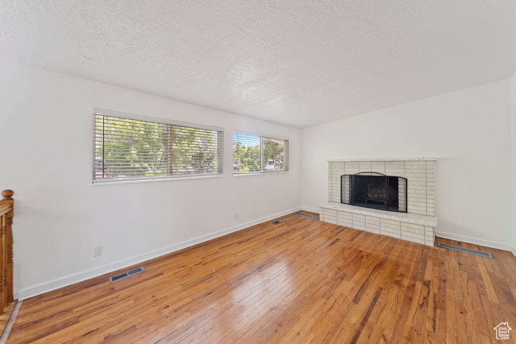Unfurnished living room featuring hardwood / wood-style flooring, baseboards, a textured ceiling, and a fireplace