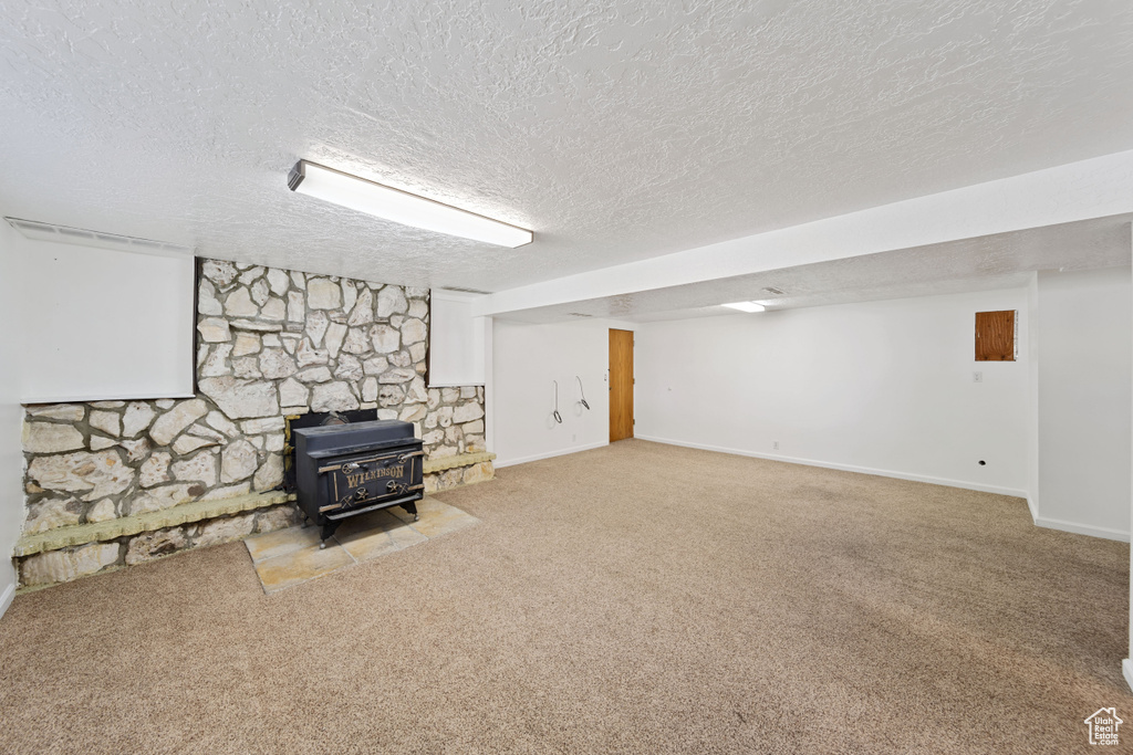 Finished basement featuring a wood stove, carpet floors, a textured ceiling, and baseboards