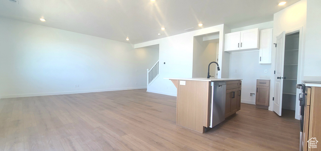Kitchen featuring an island with sink, dishwasher, light wood-style flooring, light countertops, and open floor plan