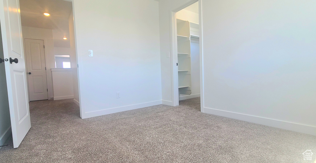 Unfurnished bedroom featuring light colored carpet, a walk in closet, baseboards, and a closet