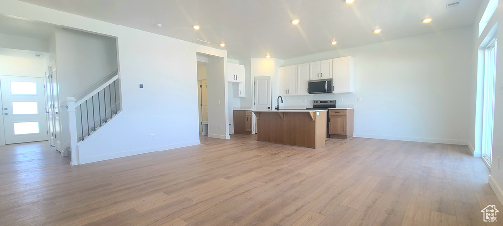 Kitchen with appliances with stainless steel finishes, open floor plan, light wood-type flooring, a kitchen island with sink, and baseboards