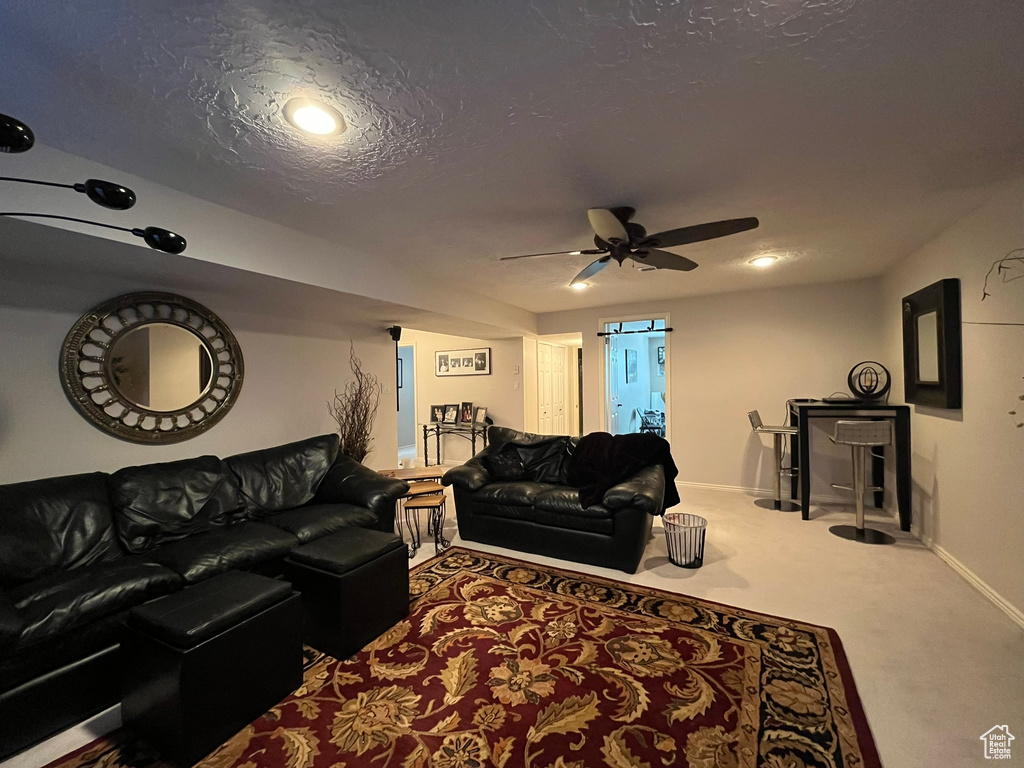 Carpeted living area with ceiling fan, baseboards, and a textured ceiling