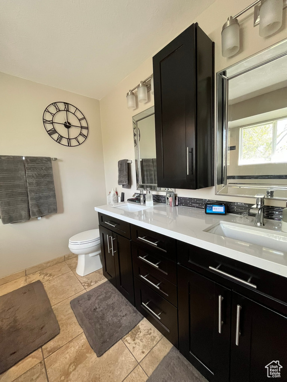 Full bath with double vanity, toilet, and tile patterned flooring