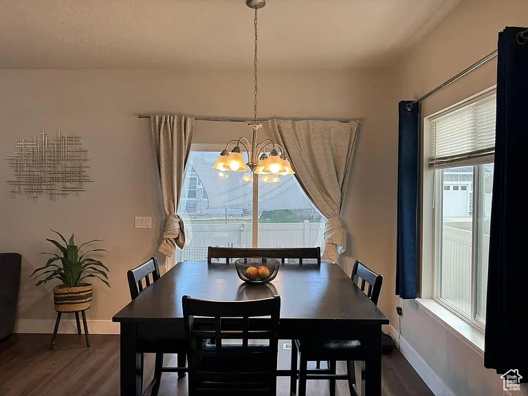Dining area featuring dark wood-style flooring, a chandelier, and baseboards