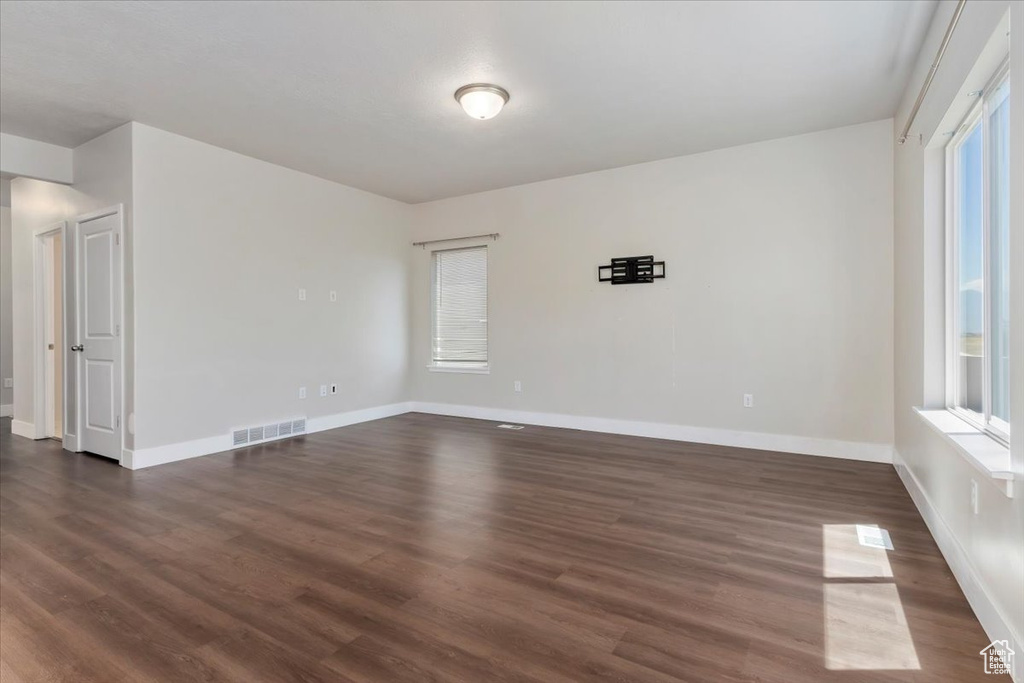 Empty room with dark wood-style flooring, baseboards, and healthy amount of natural light