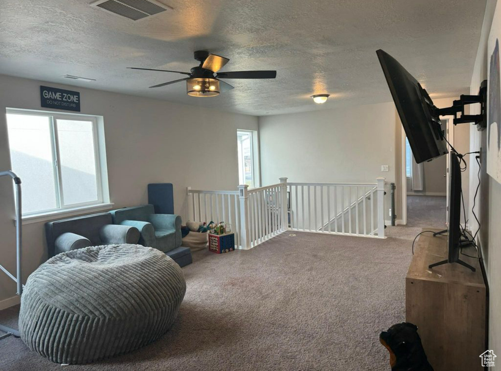 Living area featuring carpet floors, an upstairs landing, a textured ceiling, and a ceiling fan