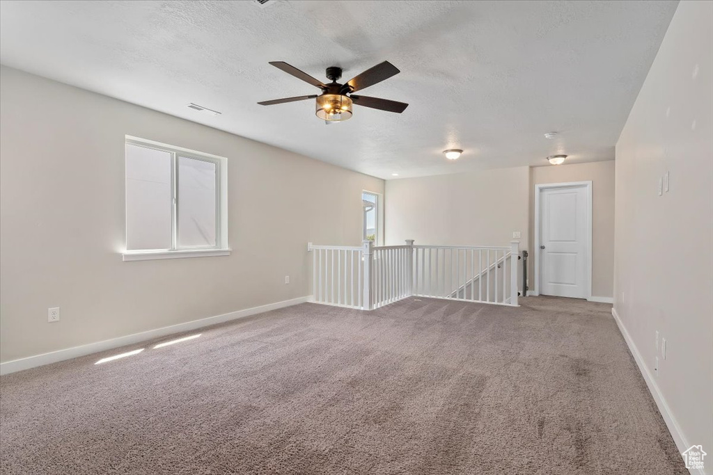 Empty room with carpet flooring, ceiling fan, baseboards, and a textured ceiling