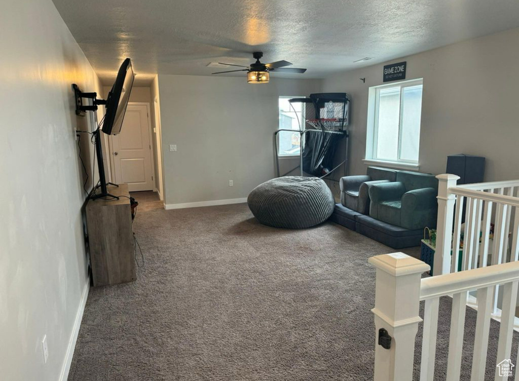 Carpeted living room featuring ceiling fan, a textured ceiling, and baseboards