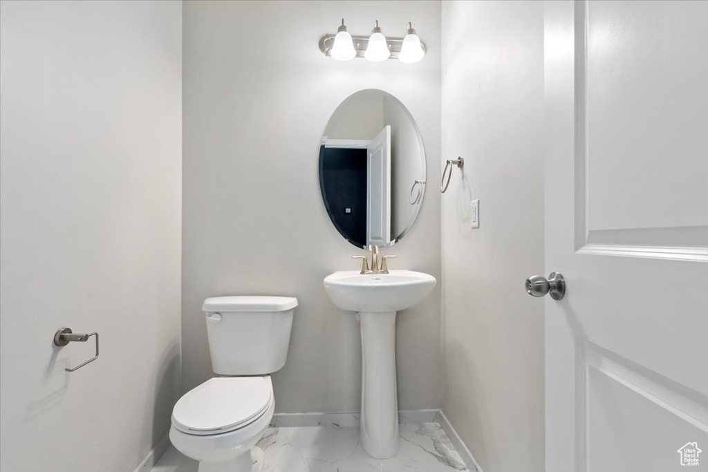 Bathroom featuring marble look tile flooring, toilet, and baseboards