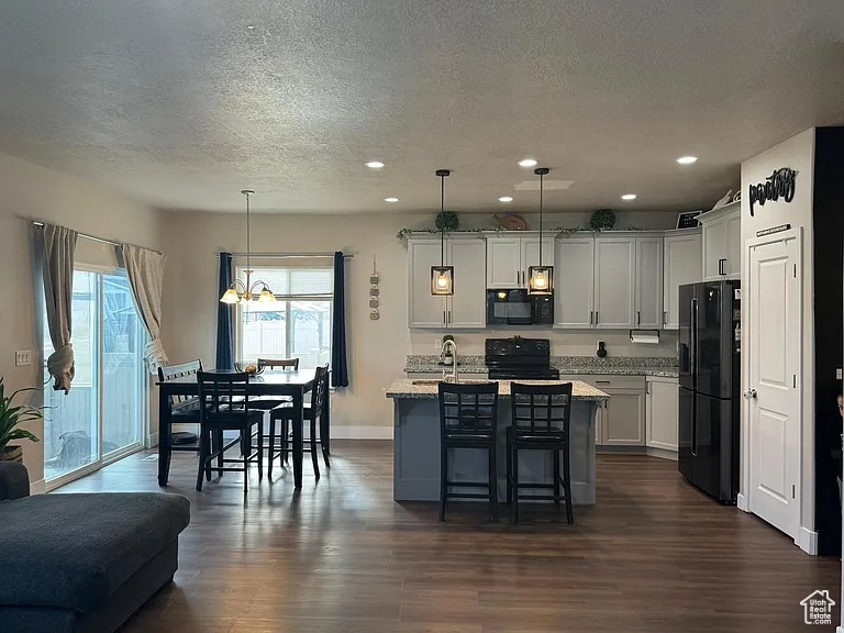 Kitchen with black appliances, a textured ceiling, dark wood finished floors, a breakfast bar area, and recessed lighting