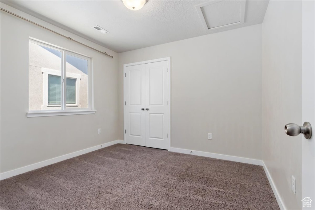 Unfurnished bedroom featuring carpet floors, baseboards, a closet, and attic access