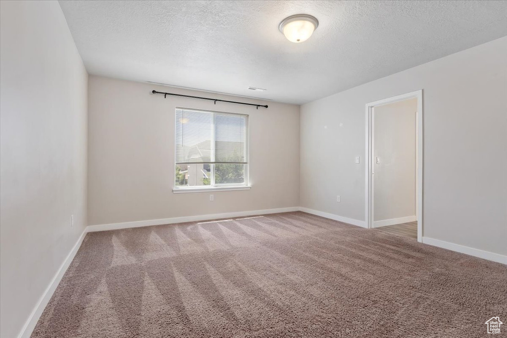 Empty room with a textured ceiling, carpet, and baseboards