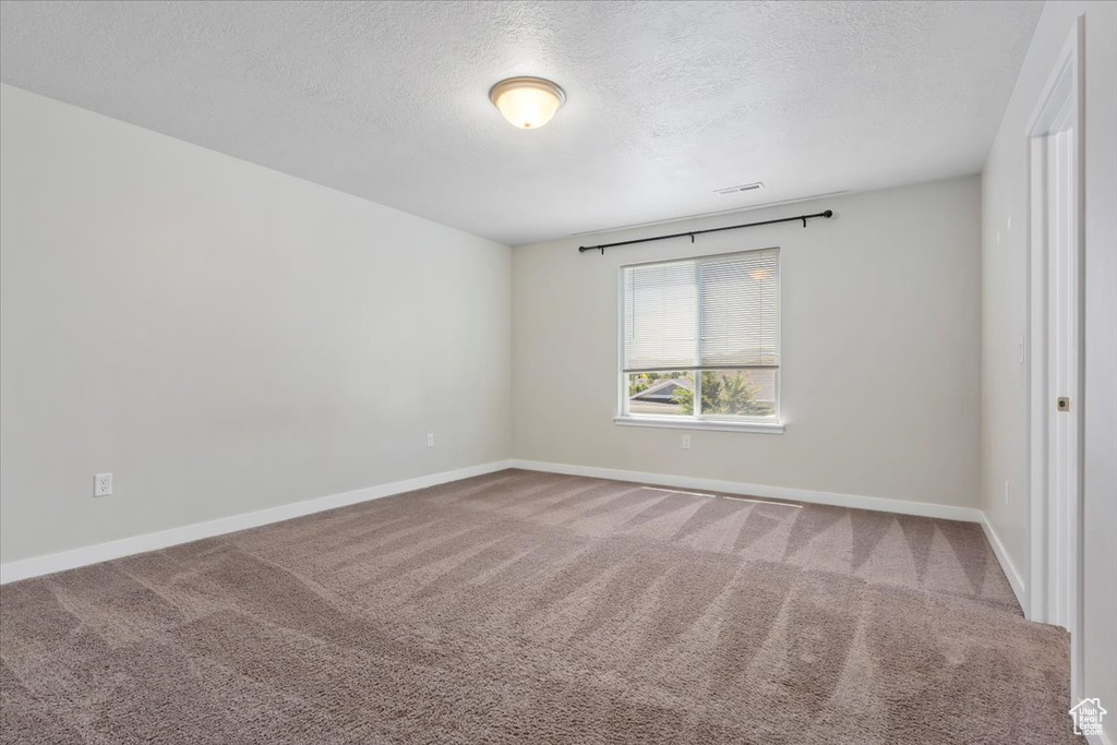 Empty room featuring a textured ceiling, carpet, and baseboards
