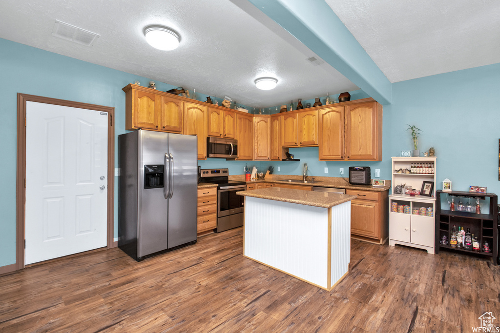 Kitchen with stainless steel appliances, a sink, dark wood-type flooring, a center island, and light stone countertops