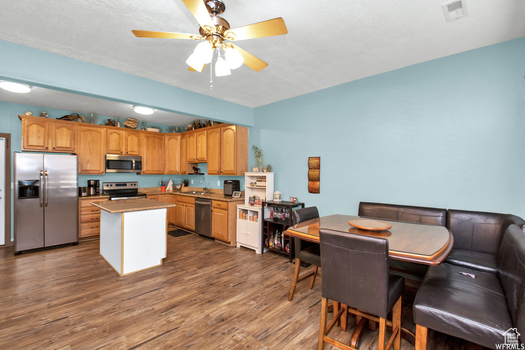 Kitchen featuring stainless steel appliances, ceiling fan, dark wood-type flooring, a center island, and a sink