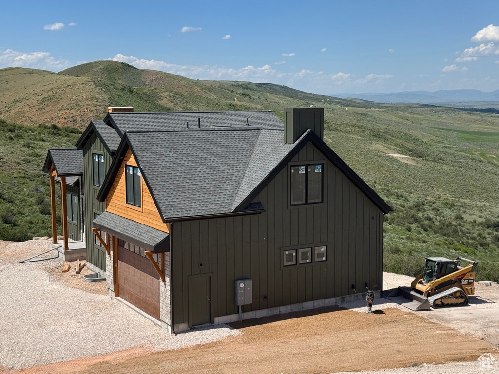 View of side of property featuring roof with shingles, a mountain view, board and batten siding, gravel driveway, and a chimney