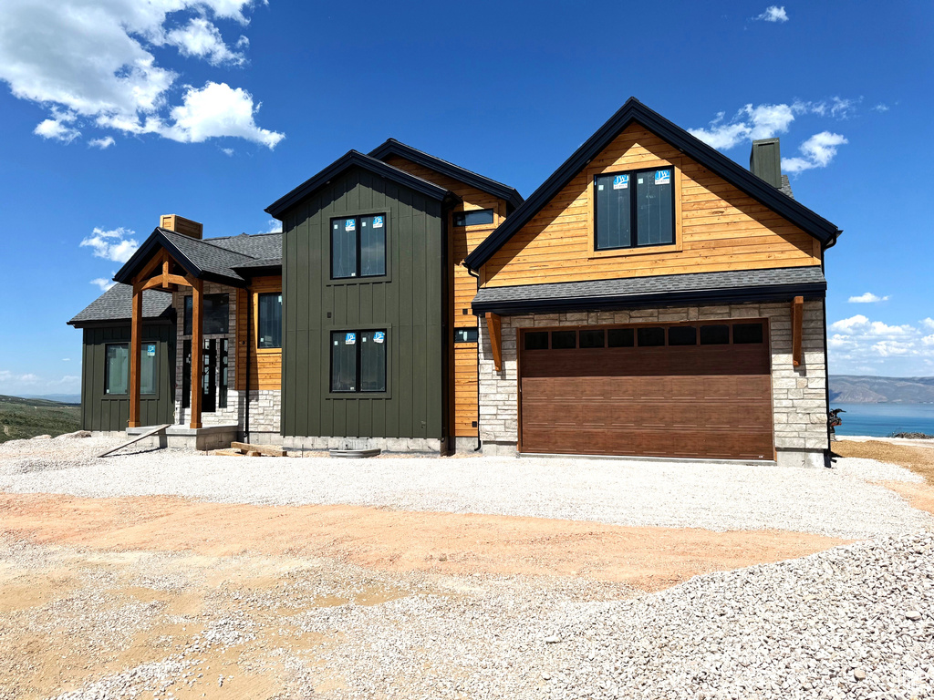 Contemporary house featuring a chimney, gravel driveway, stone siding, a shingled roof, and an attached garage