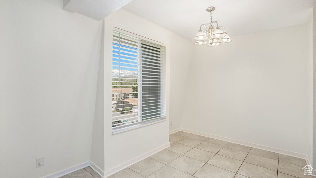 Empty room with a chandelier, baseboards, and light tile patterned flooring