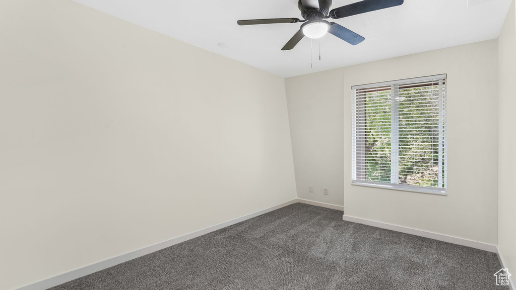 Spare room featuring plenty of natural light, dark carpet, baseboards, and ceiling fan