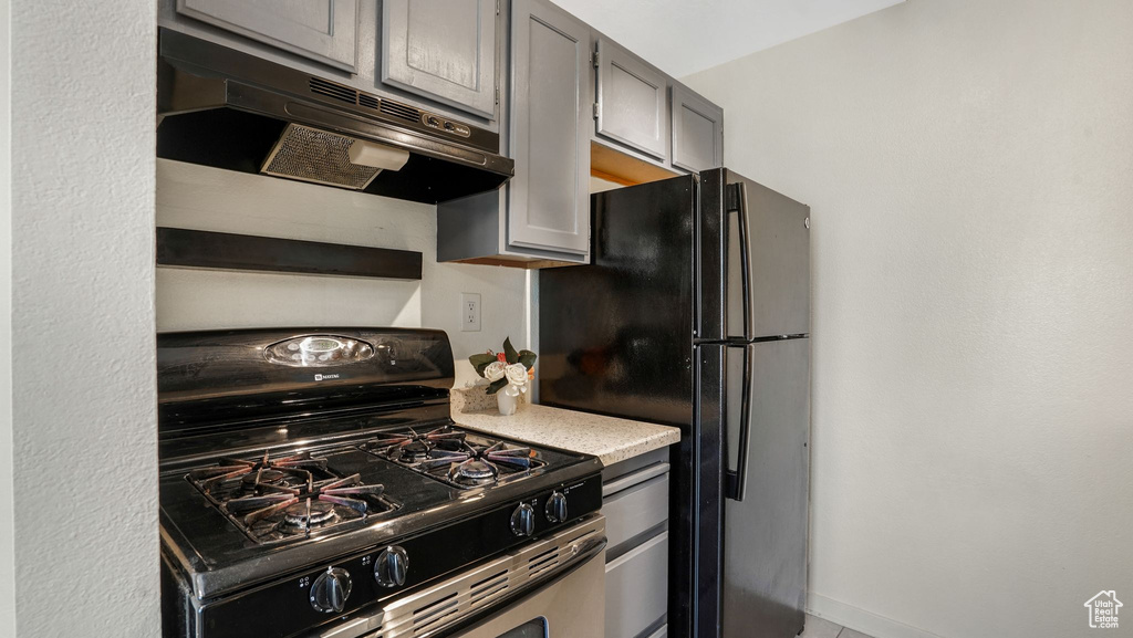 Kitchen with range with gas stovetop, under cabinet range hood, freestanding refrigerator, light countertops, and gray cabinets