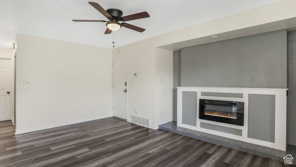 Unfurnished living room featuring dark wood-style floors, a ceiling fan, a glass covered fireplace, and baseboards
