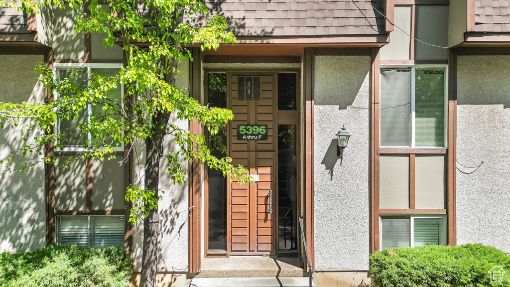 Entrance to property with stucco siding and a shingled roof