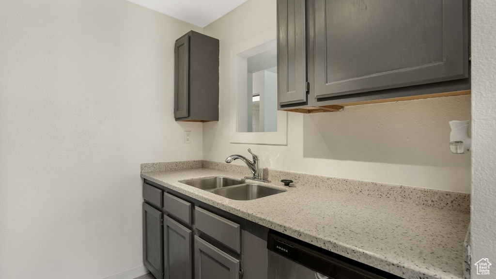 Kitchen with a sink, gray cabinetry, dishwasher, and light stone counters