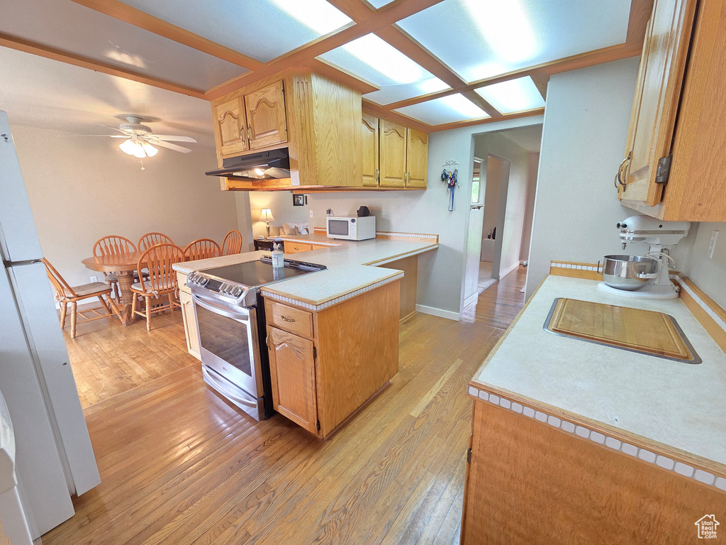 Kitchen with white appliances, under cabinet range hood, light countertops, and light wood-style flooring