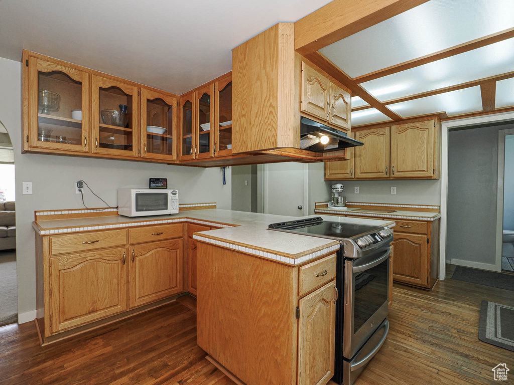 Kitchen with stainless steel range with electric stovetop, under cabinet range hood, white microwave, glass insert cabinets, and light countertops