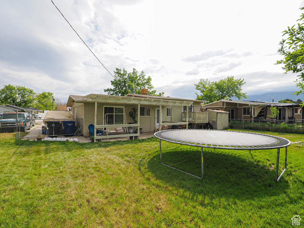 Back of house with a trampoline, a chimney, a storage unit, and an outbuilding