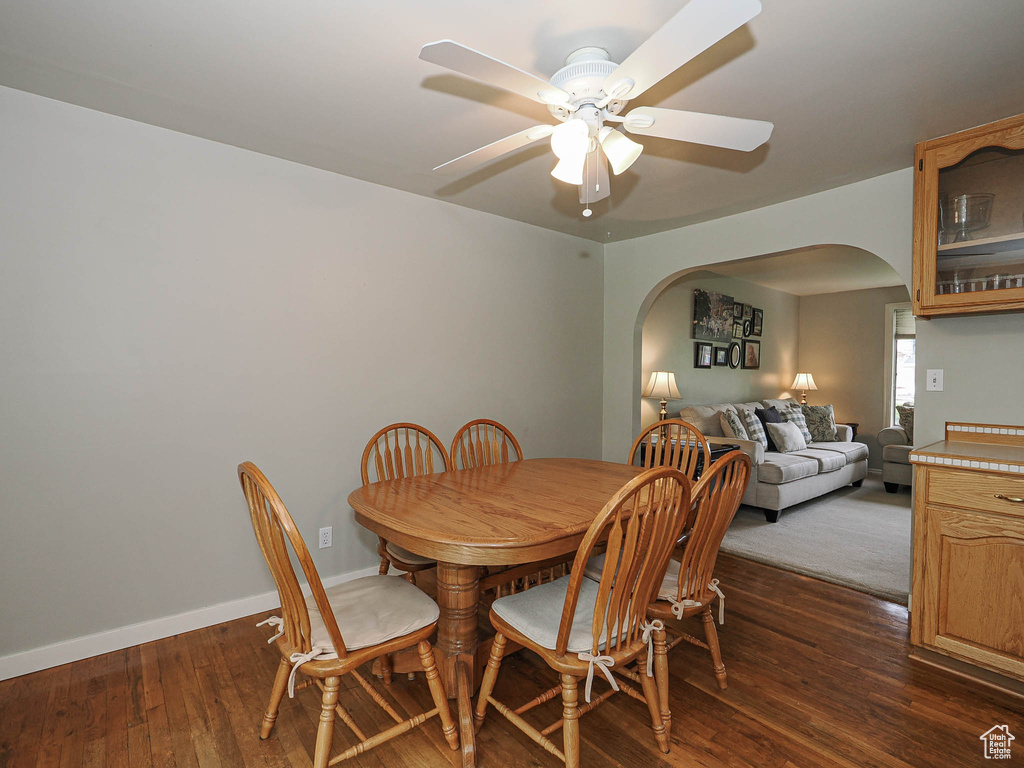 Dining area featuring arched walkways, a ceiling fan, dark wood finished floors, and baseboards