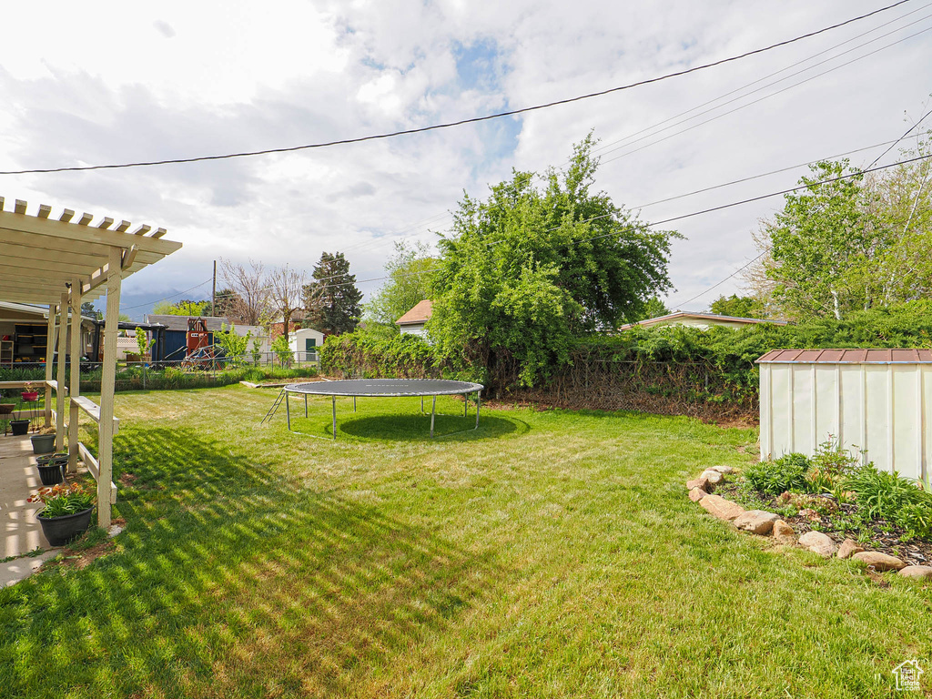 View of yard featuring a trampoline, a shed, an outdoor structure, and a pergola