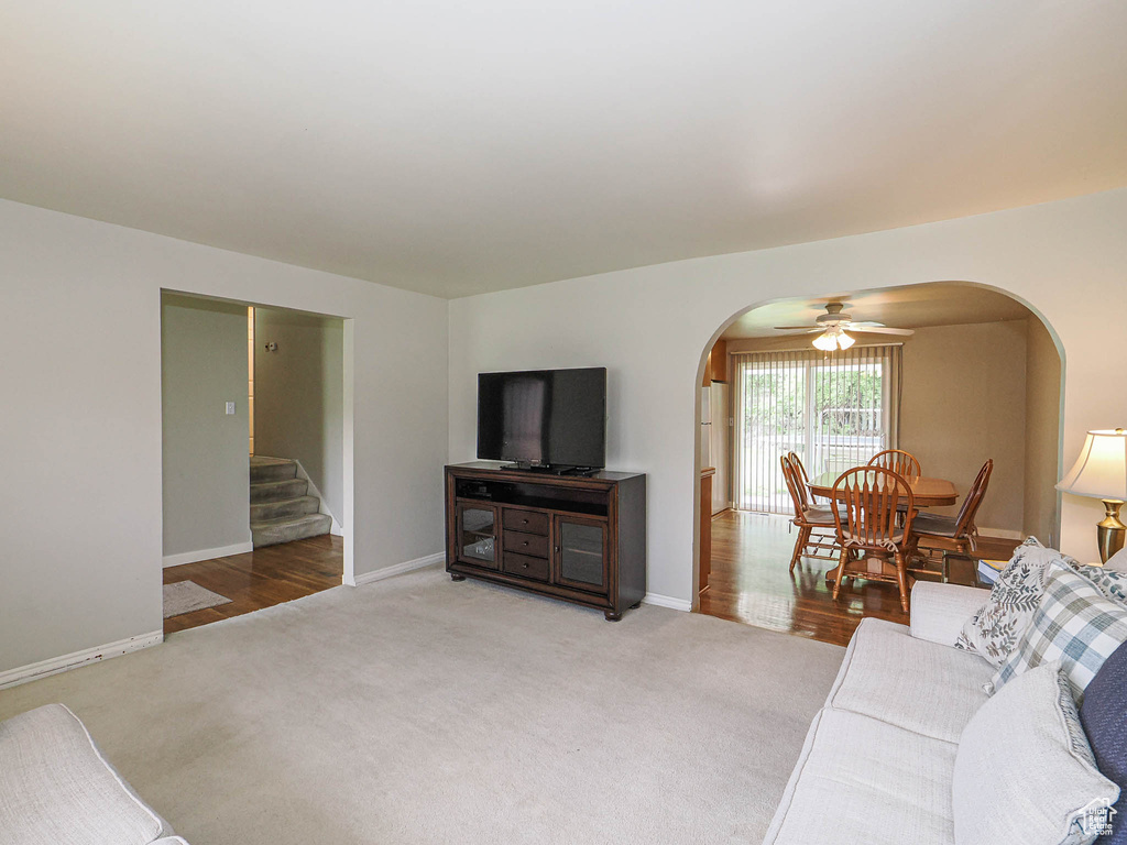 Living area featuring arched walkways, ceiling fan, stairs, and light carpet