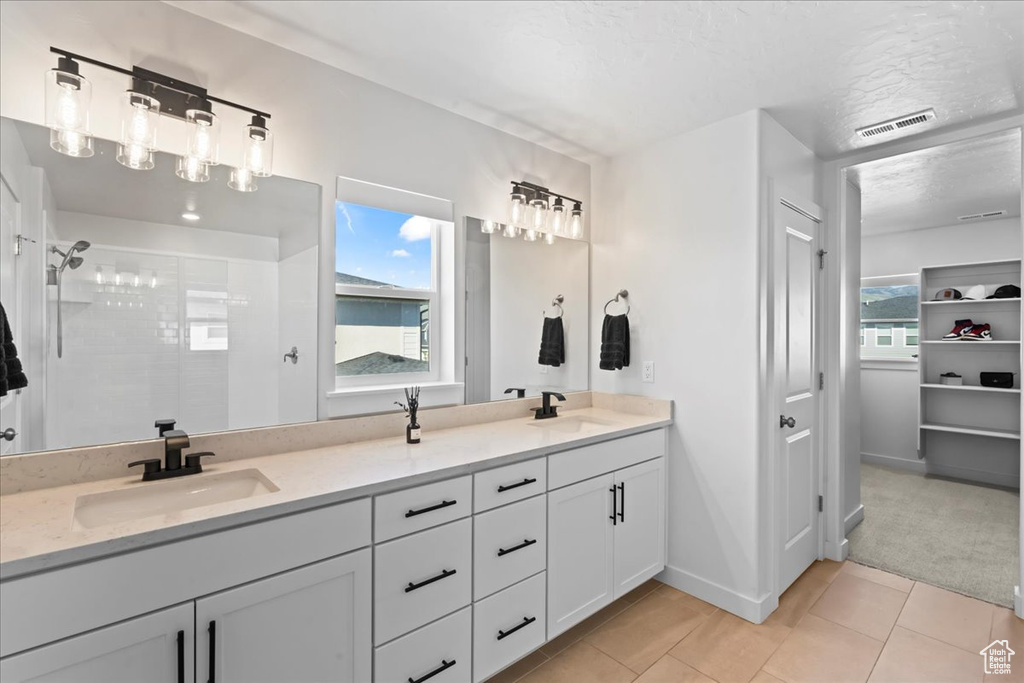 Bathroom with tile patterned floors, healthy amount of natural light, double vanity, and a tile shower