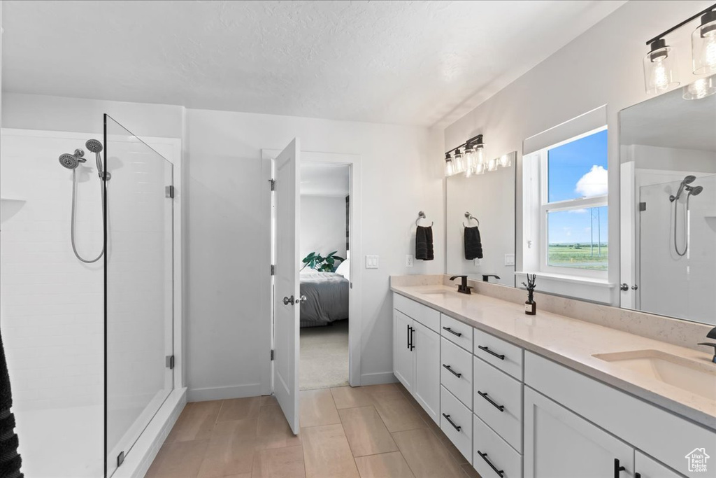 Ensuite bathroom featuring a shower stall, double vanity, and baseboards