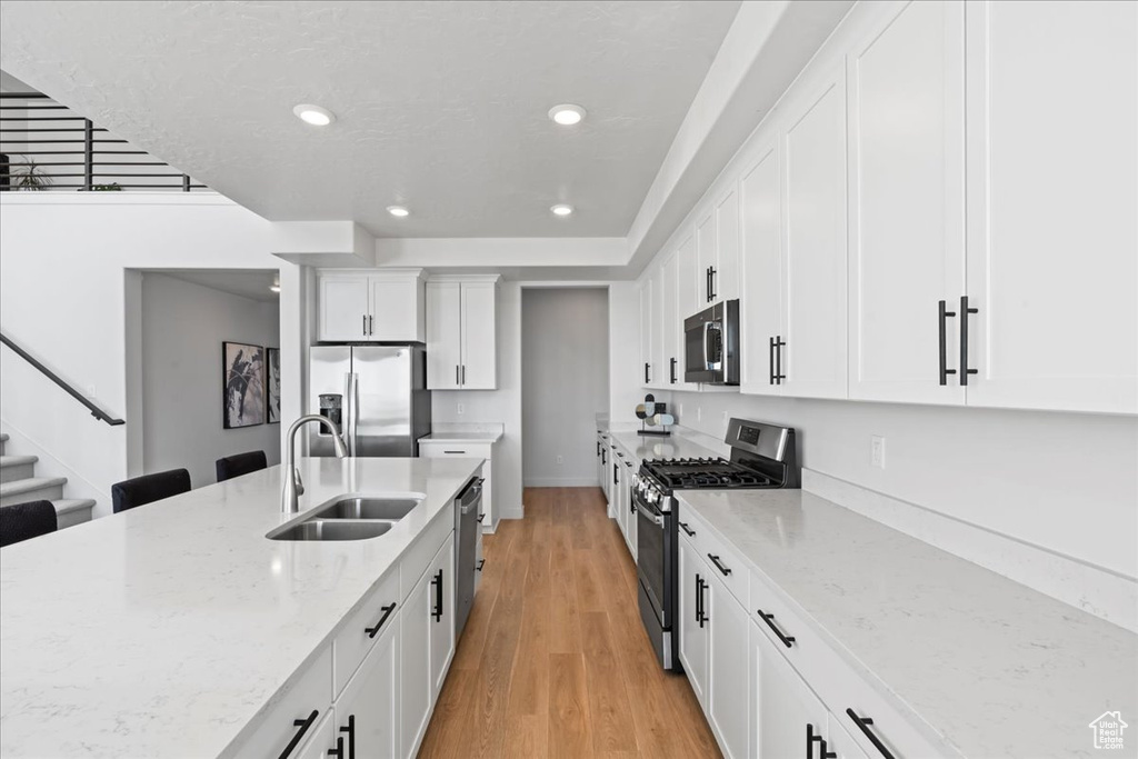 Kitchen with stainless steel appliances, a sink, recessed lighting, light wood-style floors, and white cabinetry