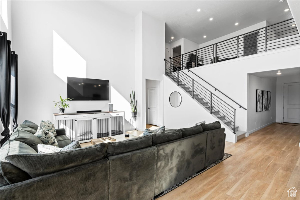Living area featuring stairs, light wood finished floors, recessed lighting, a towering ceiling, and baseboards