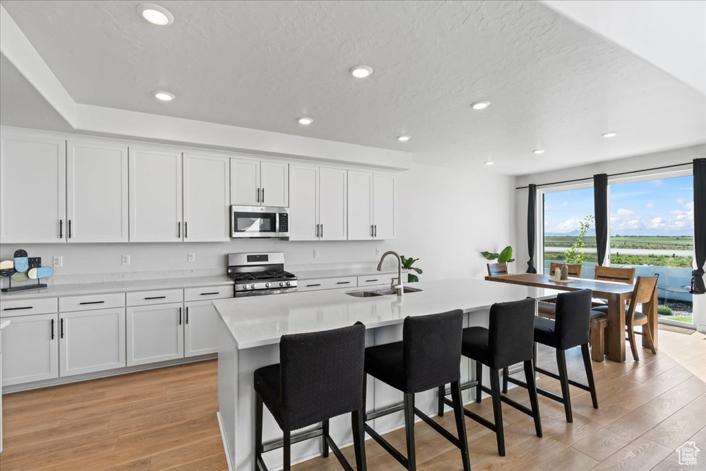 Kitchen with stainless steel appliances, a sink, light wood-style floors, a breakfast bar, and recessed lighting