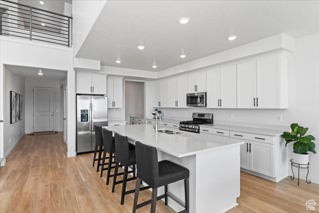 Kitchen featuring stainless steel appliances, a sink, light wood-style flooring, a kitchen breakfast bar, and white cabinets