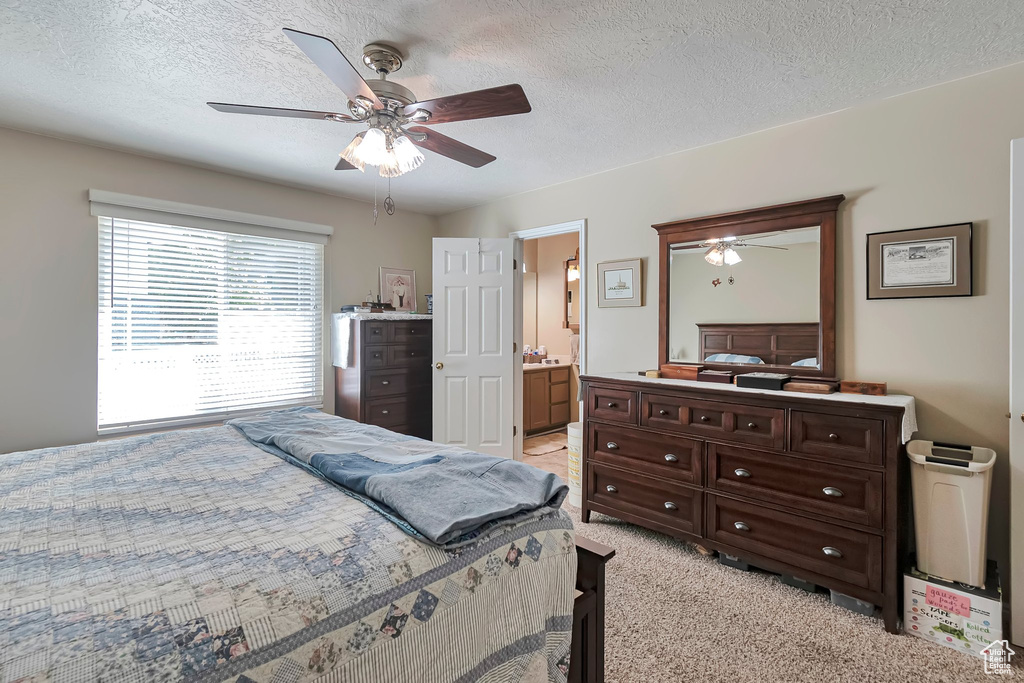 Bedroom with a textured ceiling, light colored carpet, a ceiling fan, and ensuite bathroom