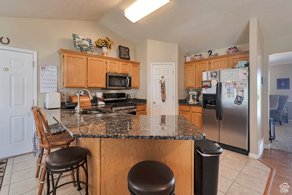 Kitchen featuring stainless steel appliances, lofted ceiling, a sink, a peninsula, and a breakfast bar