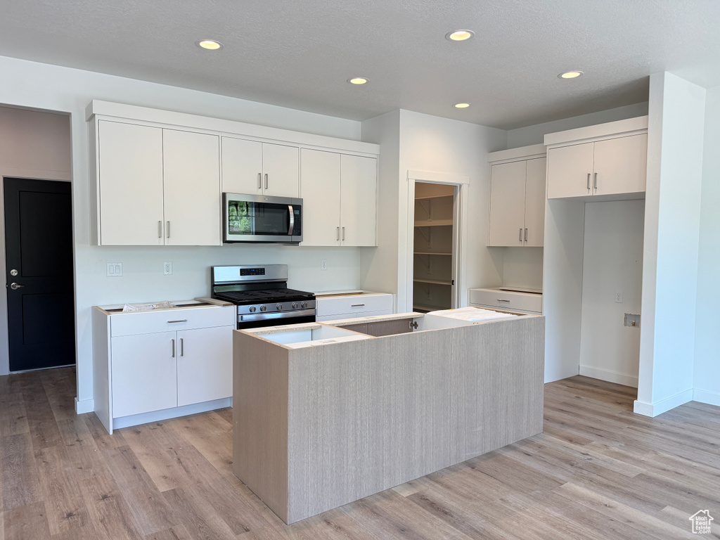 Kitchen with stainless steel appliances, a kitchen island, light wood-style floors, white cabinetry, and recessed lighting