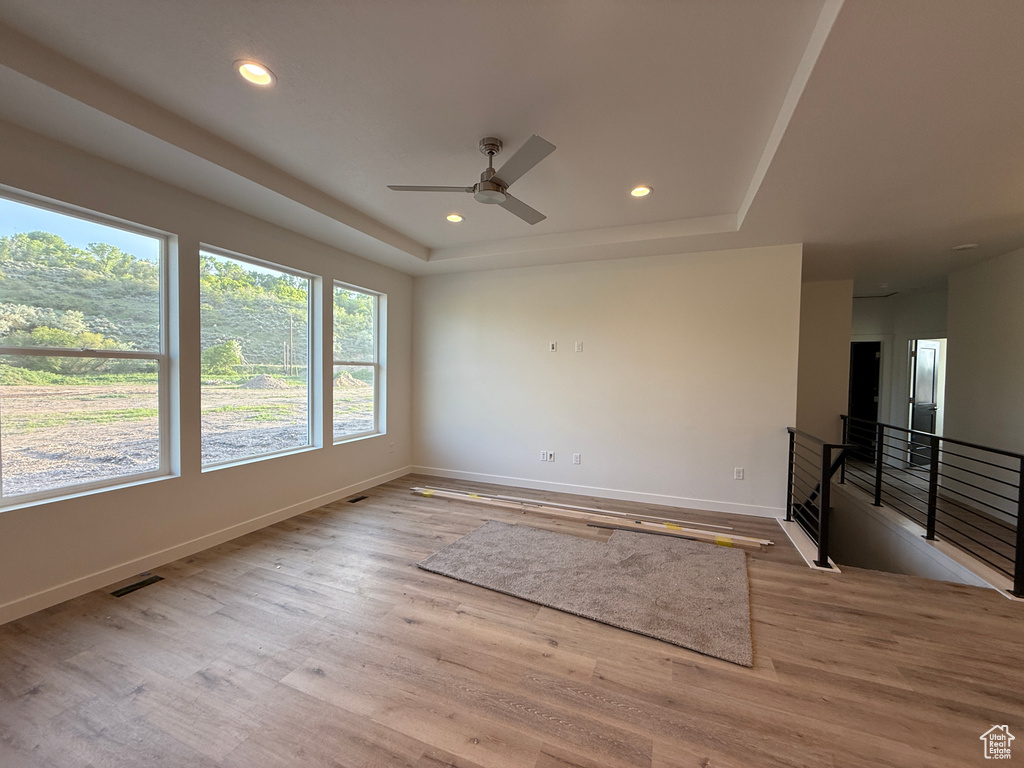 Unfurnished room with a tray ceiling, baseboards, wood finished floors, recessed lighting, and ceiling fan