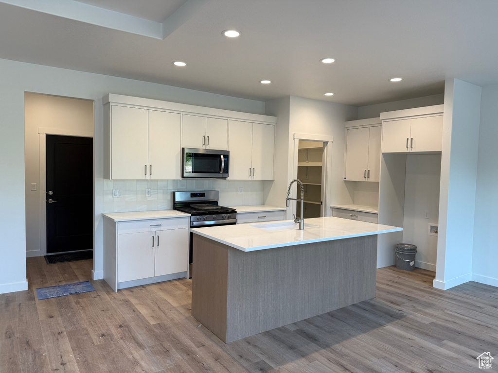 Kitchen featuring appliances with stainless steel finishes, a sink, white cabinetry, decorative backsplash, and a kitchen island with sink