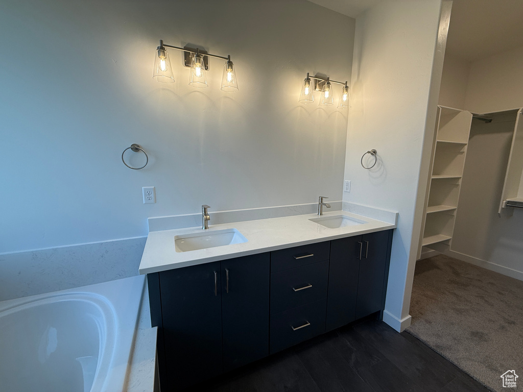 Bathroom with double vanity, a spacious closet, a tub to relax in, and baseboards