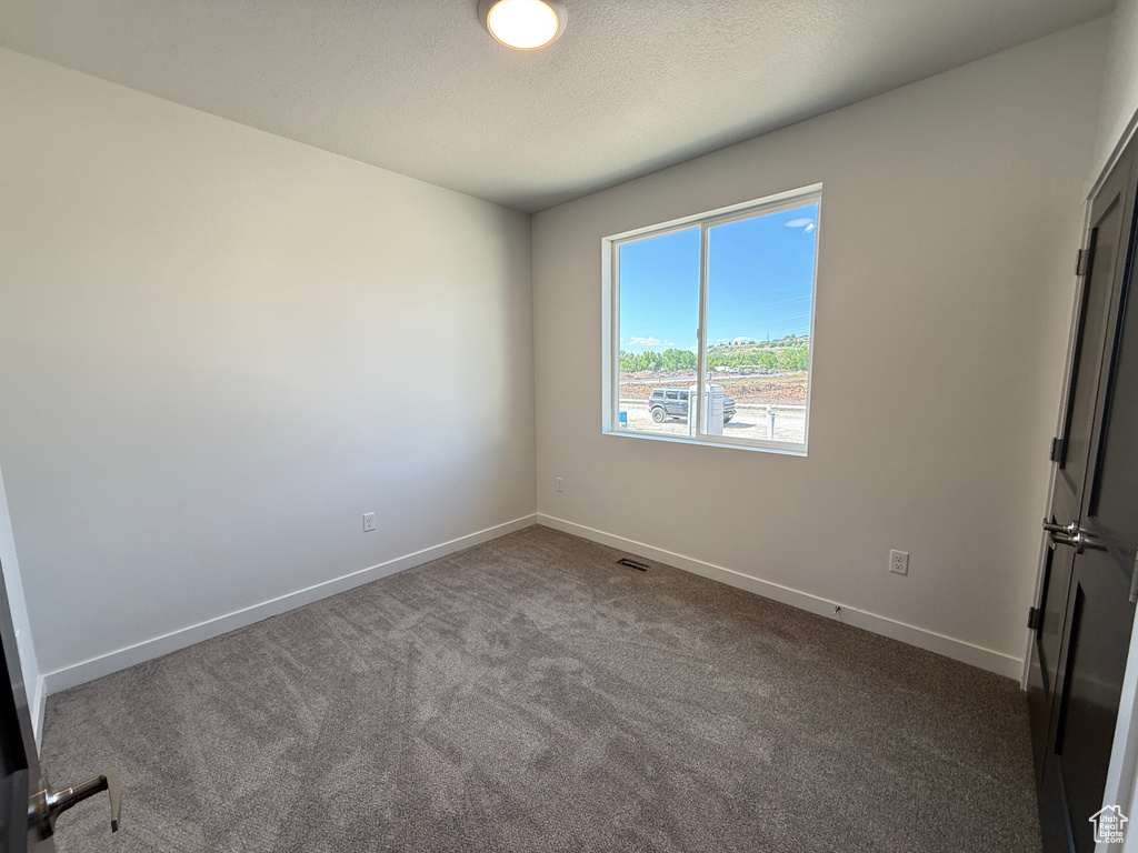 Spare room with dark carpet, baseboards, and a textured ceiling