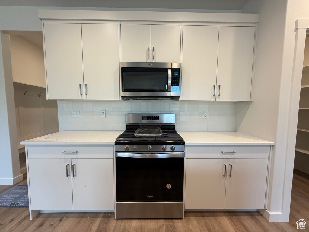 Kitchen featuring appliances with stainless steel finishes, light wood-style floors, light countertops, and white cabinets