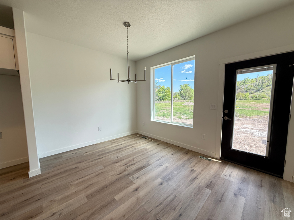 Unfurnished dining area with a chandelier, light wood finished floors, baseboards, and a textured ceiling