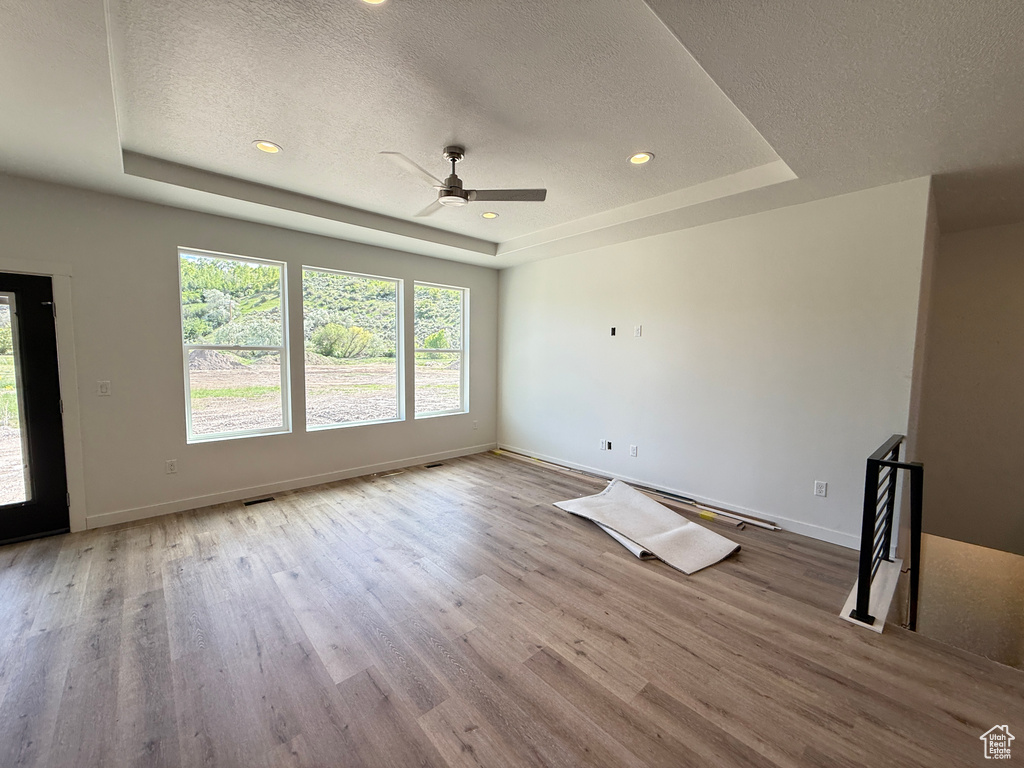 Unfurnished living room featuring a raised ceiling, a textured ceiling, wood finished floors, ceiling fan, and baseboards