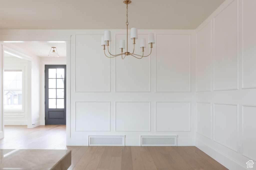Unfurnished dining area featuring a chandelier, a decorative wall, and wood finished floors